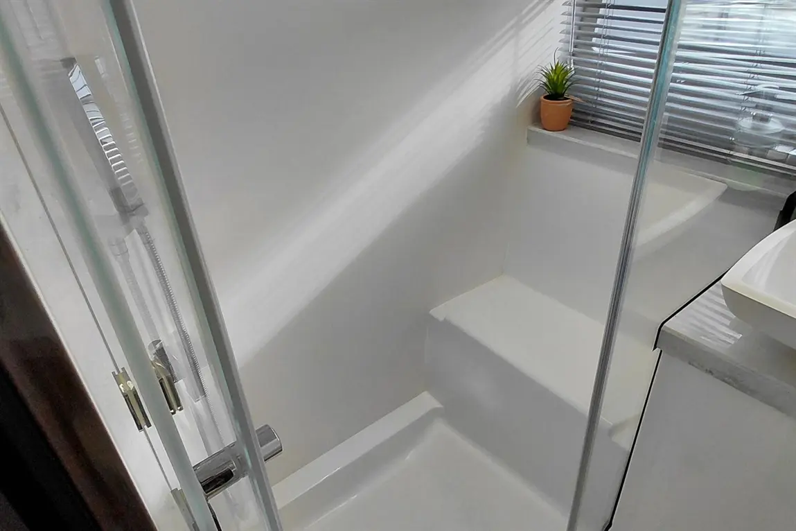 Modern shower cubicle with a sleek design, featuring glass doors, a small potted plant, and ample natural light.